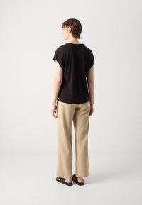 Top nero a maniche corte con vestibilità rilassata, abbinato a pantaloni beige a gamba larga e sandali neri. Design minimalista, texture liscia.