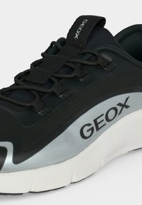 Baskets noires avec semelle blanche épaisse, bande grise sur le côté, lacets noirs et logo « "GEOX" » sur la languette et le côté.