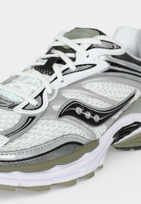 Λευκό και μαύρο αθλητικό παπούτσι Saucony με επάνω μέρος από δίχτυ, πλαστικές επικαλύψεις και μαλακή σόλα, εμφανιζόμενο από πλάγια γωνία.