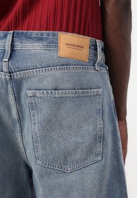 Light blue denim jeans with a brown leather patch labeled "JACK & JONES." Features include back pocket stitching and a classic cut.
