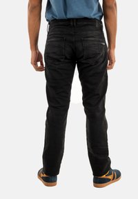 Vaqueros de mezclilla negros con corte ajustado, que cuentan con bolsillos traseros y detalles sutiles, combinados con zapatillas de rayas azul marino y naranja.