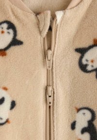 Beige fleece zip-up beklædning med pingvinmønstre i sort, hvid og orange. Blød tekstur med en central lynlåslukning.