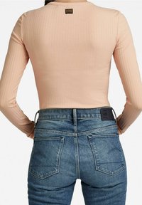 Bluzka z długim rękawem o prążkowanej fakturze w jasnopomarańczowym kolorze, zestawiona z niebieskimi, wysokim stanem dżinsami z tylnymi kieszeniami i czarną naszywką z logo.