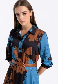 Sukienka w kwiatowy wzór z kołnierzykiem, w odcieniach niebieskiego i brązowego. Posiada guziki oraz brązowy pasek w talii. Gładka faktura materiału.