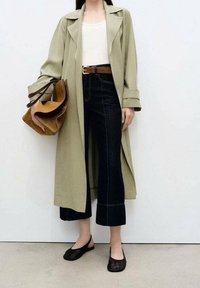 Długi oliwkowozielony płaszcz, biały top, ciemne spodnie jeansowe o kroju cropped z kontrastującym przeszyciem, brązowy pasek, brązowa torba wielokomorowa, czarne baleriny.