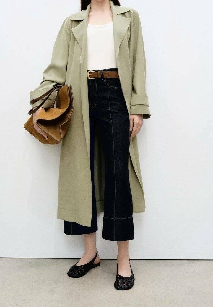 Długi oliwkowozielony płaszcz, biały top, ciemne spodnie jeansowe o kroju cropped z kontrastującym przeszyciem, brązowy pasek, brązowa torba wielokomorowa, czarne baleriny.