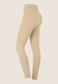 Leggings beige con una trama liscia, vita alta e due tasche posteriori. Presentano cuciture sottili e accenti in hardware dorato.