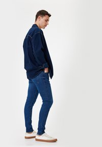 Camisa vaquera azul de manga larga, de corte holgado. Combinada con unos jeans skinny azul oscuro y zapatillas blancas con detalles marrones.