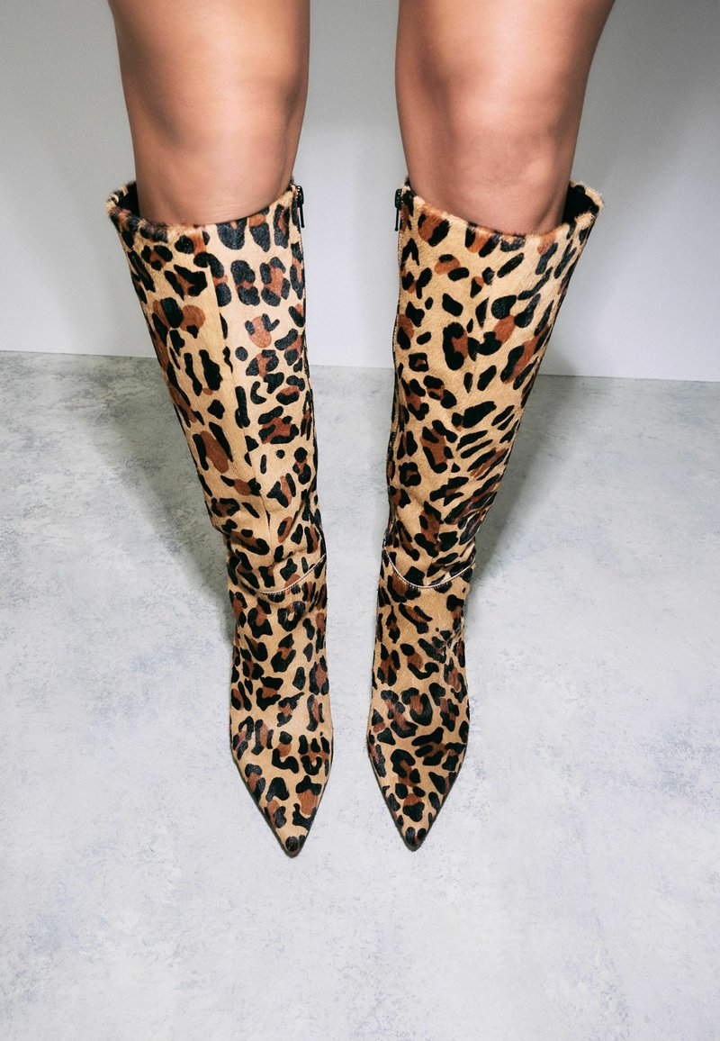 Bottes montantes en imprimé léopard avec bouts pointus, fabriquées en matériau doux, dotées de fermetures éclair à l'arrière et d'un design ajusté.