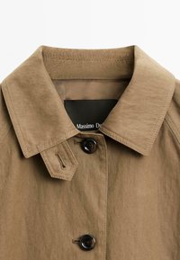 Bruine colbert met twee zwarte knopen en een gestikte riemdetails nabij de kraag, met een "Massimo Dutti" label aan de binnenkant.