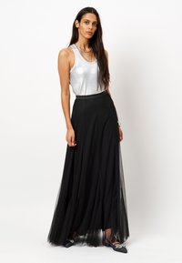 Zilveren mouwloze top met een glinsterende afwerking, gecombineerd met een lange, vloeiende zwarte tule rok. Zwarte schoenen met decoratieve accenten maken de outfit compleet.