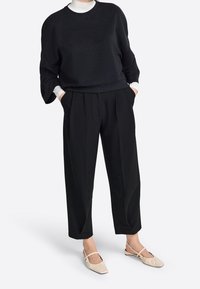 Svart oversized sweatshirt med dolmansärmar, matchad med skräddarsydda svarta byxor med veck. Ljust beige slingback-skor.