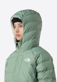 Roheline puffer-jope kapuutsiga, millel on tõmblukuga sulgur ja North Face'i logo. Tekstuuriga kangas horisontaalsete õmblustega isoleerimiseks.