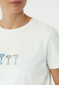 Witte, korte mouwen t-shirt met een gedrukt ontwerp van vier verschillende cocktailglazen in diverse kleuren en stijlen over de borst.