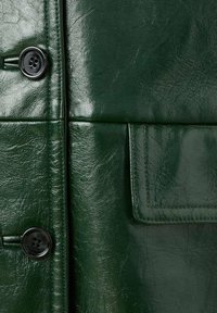 Giacca in pelle verde scuro con una texture lucida, caratterizzata da una chiusura con bottoni neri e una tasca laterale con dettaglio di bordi cuciti.