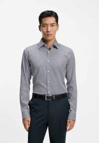 Gestreept overhemd in marineblauw en wit, met een button-down kraag, lange mouwen en een getailleerde pasvorm. Gecombineerd met een donkere broek en een riem.