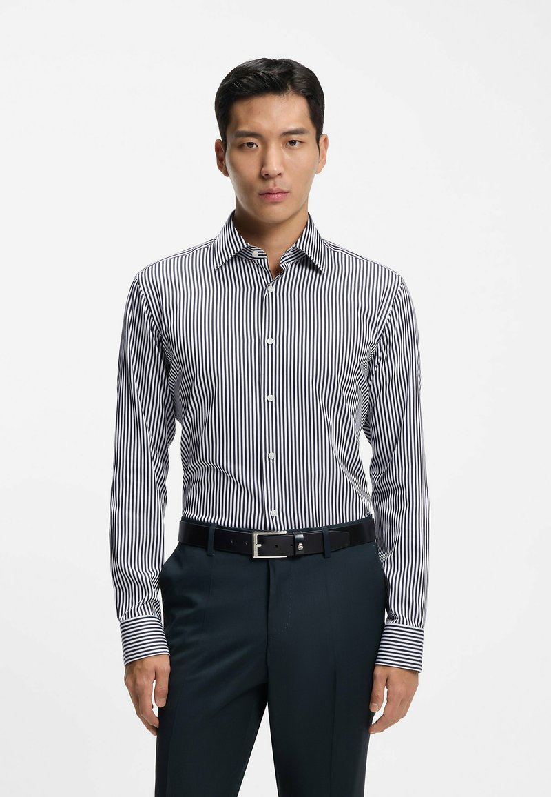 Gestreept overhemd in marineblauw en wit, met een button-down kraag, lange mouwen en een getailleerde pasvorm. Gecombineerd met een donkere broek en een riem.