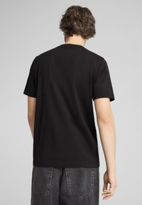 Camiseta de algodón negra con mangas cortas, cuello redondo y una textura suave. Llevada con pantalones cortos de corte relajado en gris oscuro.