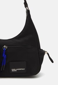 Črna najlonska torba za ramo z ukrivljeno zasnovo, z zadrgo, modrim vrvicama in oznako blagovne znamke Karl Lagerfeld Jeans.