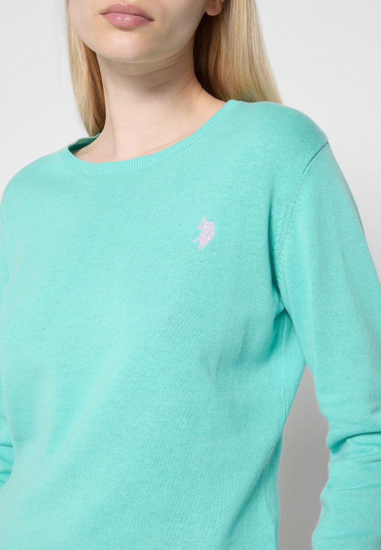 Helles Türkis Sweatshirt mit rundem Ausschnitt, gestrickter Textur und einem kleinen rosa gestickten Logo auf der linken Brustseite.