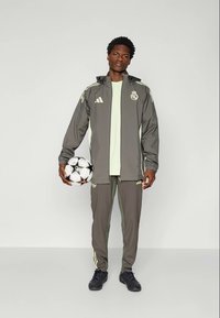 Veste de sport grise avec des accents vert clair, pantalons assortis et chaussures de foot noires ; tenant un ballon de football noir et blanc.