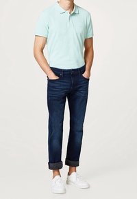 Ljusblå trapetsfärgad skjorta, mörkblå jeans med uppvikta ben, och vita sneakers. Polotröjan har en klassisk passform och jeansen har en denimstruktur.