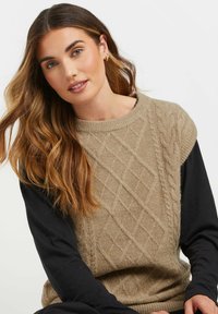 Maglione lavorato a maglia di colore marrone chiaro con un motivo a diamante testurizzato, abbinato a una camicia nera a maniche lunghe. Collo a costine e texture morbida.