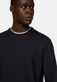 Navy ribbed knit sweater with a crew neckline, featuring a white inner collar detail and a close-fitting silhouette.