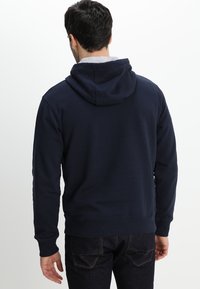 Sudadera azul marino hecha de una mezcla de algodón, con una textura suave, capucha con cordones y puños y dobladillo acanalados. La vista posterior no muestra gráficos.