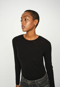 Zwarte langemouwen top met een ronde halslijn, gemaakt van zachte stof. Het model draagt hooggewijze grijze jeans, die een minimalistisch ontwerp tonen.