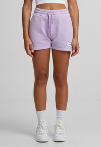 Lila bomullsshorts med elastisk midjeband, dragsko och broderad logotyp på nederdelen av benet. I kombination med vita strumpor och sneakers.