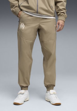 Beżowe spodnie sportowe o wąskim kroju, z elastycznymi mankietami i detalem z logo. Wykonane z gładkiego, lekkiego materiału z dodatkowymi akcentami przy bocznych kieszeniach.
