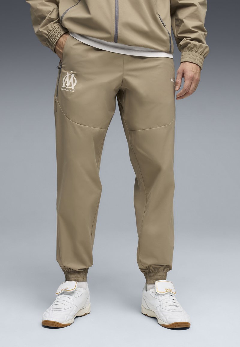 Μπεζ αθλητικό παντελόνι με στενή εφαρμογή, ελαστικές μανσέτες και λεπτομέρεια με λογότυπο. Διαθέτει λείο, ελαφρύ ύφασμα με διακριτικές τσέπες στο πλάι.