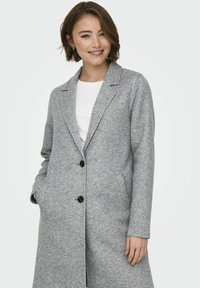 Manteau en mélange de laine gris avec un revers en dent de scie, deux poches avant et des boutons noirs, présentant un design structuré légèrement texturé.