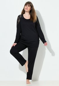 Conjunto de loungewear negro que incluye una camiseta de manga larga con detalles de encaje, un top de corte relajado y pantalones a juego con una textura suave.