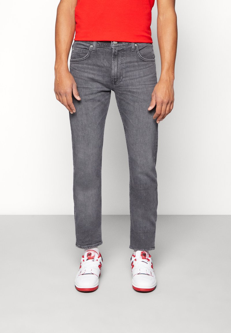 Gray denim jeans with a slim fit, five-pocket design, and subtle stitching details, paired with white sneakers featuring red accents.
