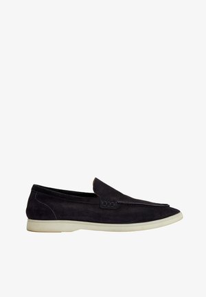 Sort ruskind slip-on loafer med hvid gummisål, lav hæl og minimalistisk design.