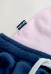 Nærbillede af pink stof med marineblå "Superdry" mærkat ved siden af marineblåt ribbet stof med hvid snor.