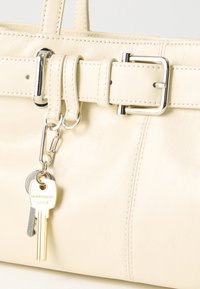 Μπεζ δερμάτινη τσάντα με ραμμένες λεπτομέρειες, ασημένια αγκράφα και δύο κλειδιά κρεμασμένα από μεταλλικό κλιπ στον κρίκο της ζώνης.