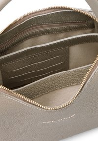 Intérieur d'un sac à main en cuir gris clair avec plusieurs compartiments, une poche zippée et des emplacements pour cartes. Détails en zip doré et texture subtile.