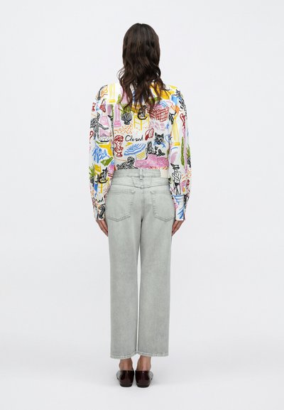 Chemise graphique multicolore à manches longues, associée à un jean large gris clair et des chaussures marron foncé, vue de dos.