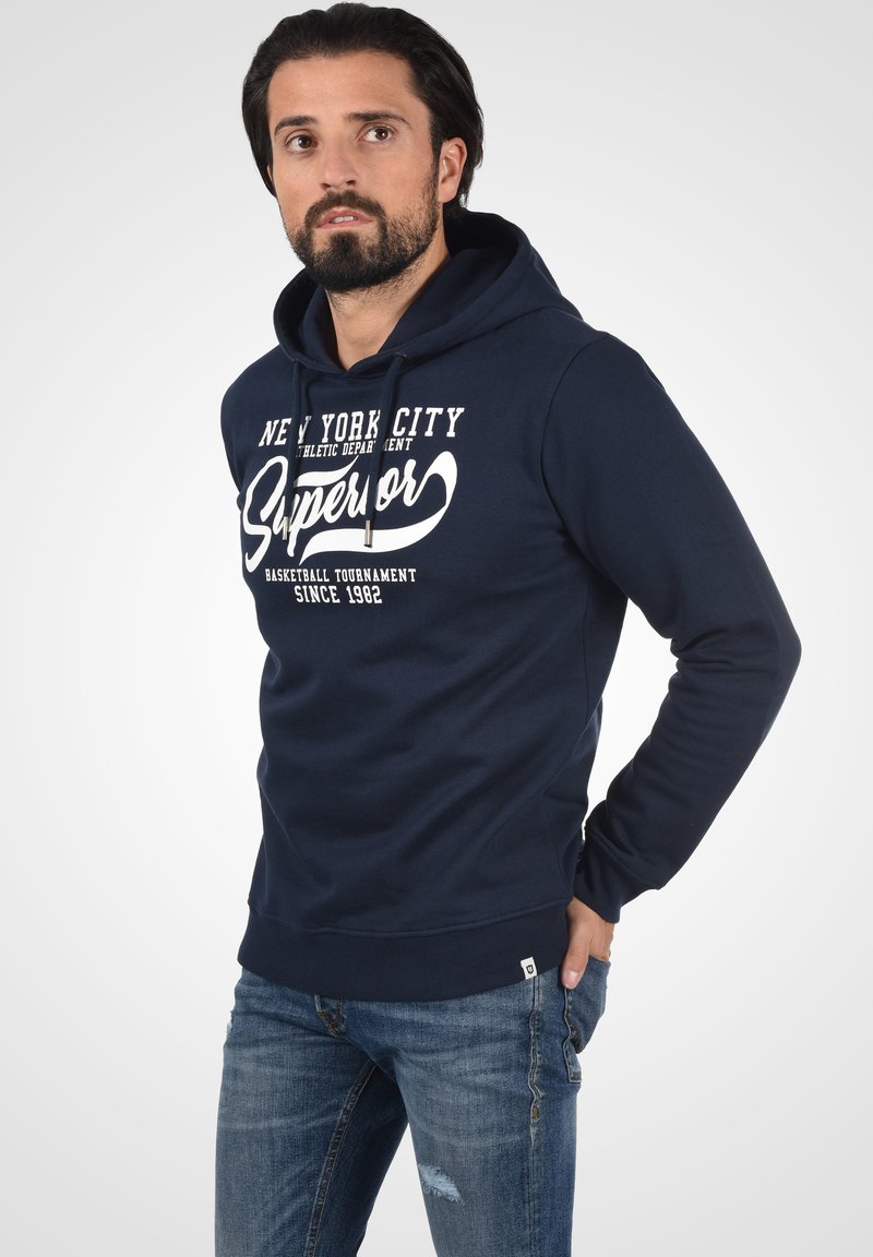 Marineblauwe hoodie met witte opdruk "New York City Superior." Beschikt over een voorzak in kangoeroestijl en geribbelde manchetten.