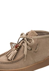 Chaussure cheville en daim marron clair avec fermeture à lacets à l'avant, pompons décoratifs et perles, et étiquette latérale de marque sur une semelle en caoutchouc beige.