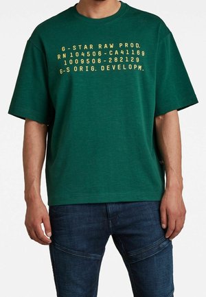 Zielona bawełniana koszulka z krótkimi rękawami, z żółtym napisem: "G-STAR RAW PROD." oraz szczegółami numerycznymi. Prosty krój, casualowy fason.