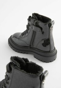Bottes en cuir verni noir avec une finition texturée, dotées d'une fermeture éclair, de détails en lacets et d'un col doublé de fourrure pour plus de chaleur.