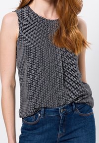 Haut sans manches Noir et Blanc avec un motif ondulé, fabriqué dans un tissu léger, associé à un jean en denim bleu.