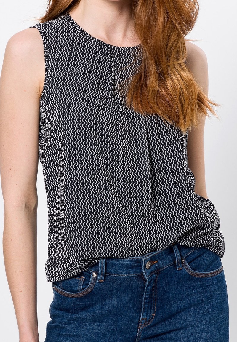 Haut sans manches Noir et Blanc avec un motif ondulé, fabriqué dans un tissu léger, associé à un jean en denim bleu.