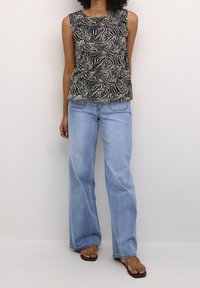 Top sans manches noir et crème avec un motif zèbre, associé à un jean bleu clair à jambes larges et des sandales marron.