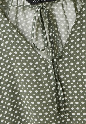 Haut à motifs verts avec un décolleté en V, en tissu léger, et des formes de diamants blancs. Des liens au cou ajoutent un détail au design.