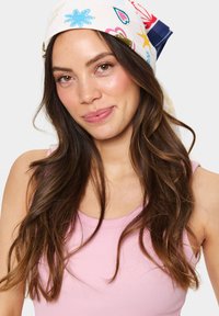 Šarena tiskana marama s cvjetnim i geometrijskim uzorcima u plavoj, ružičastoj i zelenoj boji, vezana na stražnjoj strani glave, nošena s ružičastom bluzom.